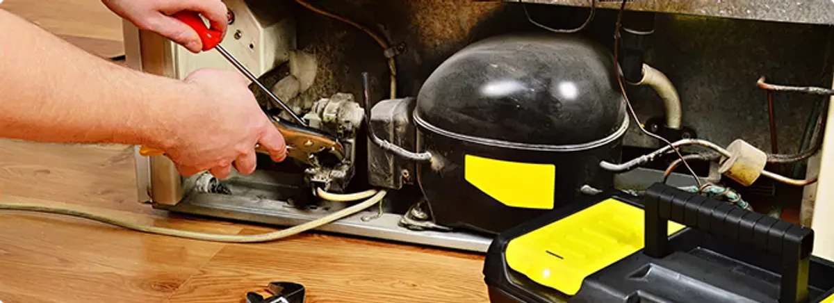 Refrigerator repair technician fixing the compressor and wiring in Fairport, NY