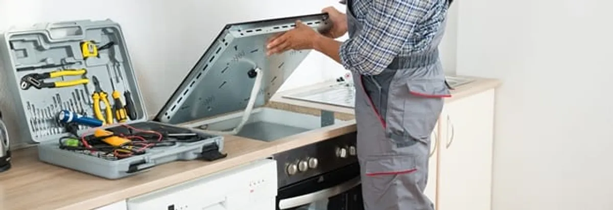 Cooktop repair technician lifting a built-in stovetop for service in Rochester, NY
