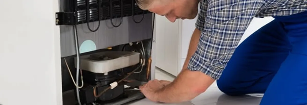 Refrigerator repair technician servicing the compressor and condenser area in Rochester, NY