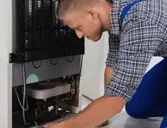 Refrigerator repair technician servicing the compressor and condenser area in Rochester, NY